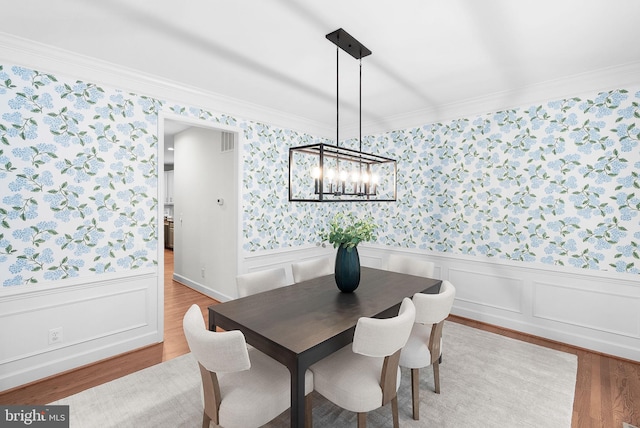 dining room with wood finished floors, visible vents, ornamental molding, wainscoting, and wallpapered walls