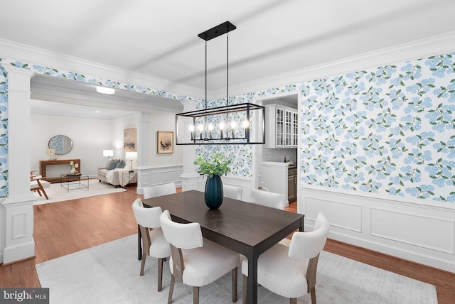 dining area with a wainscoted wall, wood finished floors, decorative columns, and crown molding