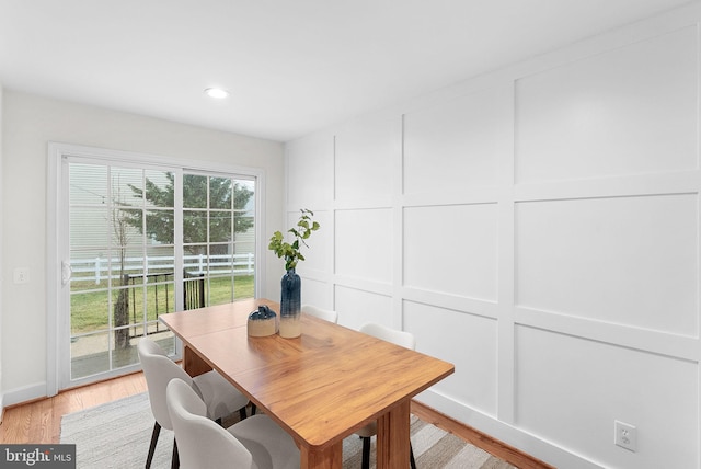 dining space with light wood finished floors, a decorative wall, and recessed lighting