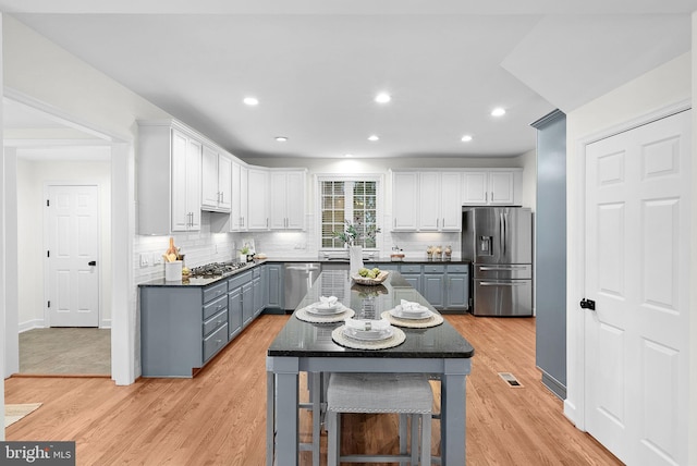 kitchen featuring light wood finished floors, white cabinets, decorative backsplash, dark countertops, and appliances with stainless steel finishes