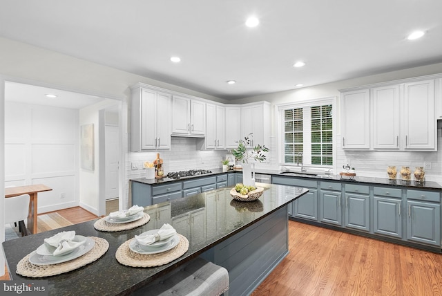 kitchen with white cabinets, light wood-style flooring, a sink, stainless steel gas cooktop, and backsplash