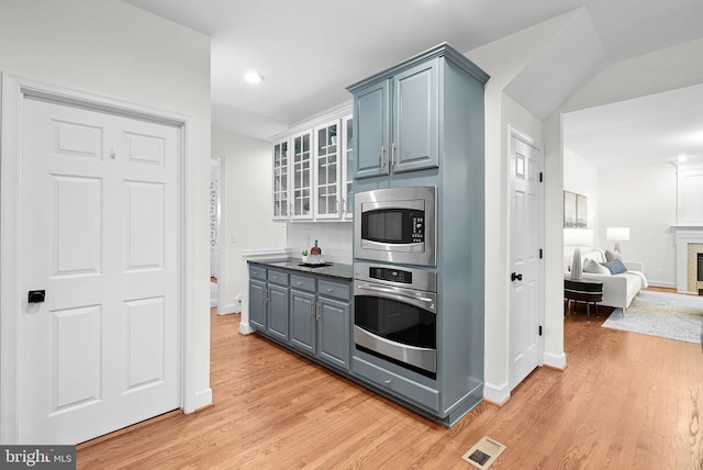 kitchen featuring stainless steel appliances, visible vents, light wood finished floors, glass insert cabinets, and tasteful backsplash