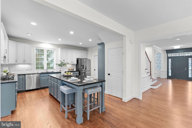 kitchen with light wood finished floors, white cabinets, dark countertops, stainless steel appliances, and a sink