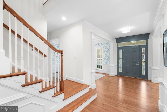 foyer entrance with ornamental molding, wood finished floors, stairs, ornate columns, and a decorative wall