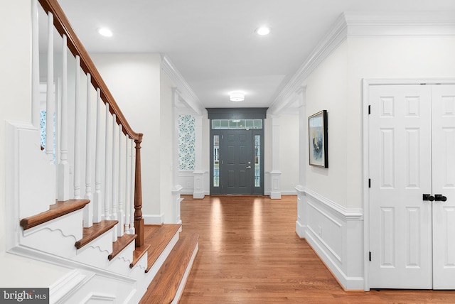 foyer with light wood finished floors, stairway, a decorative wall, and crown molding