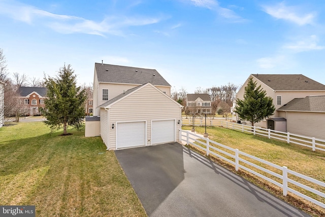 view of side of property with a garage, fence, aphalt driveway, and a yard