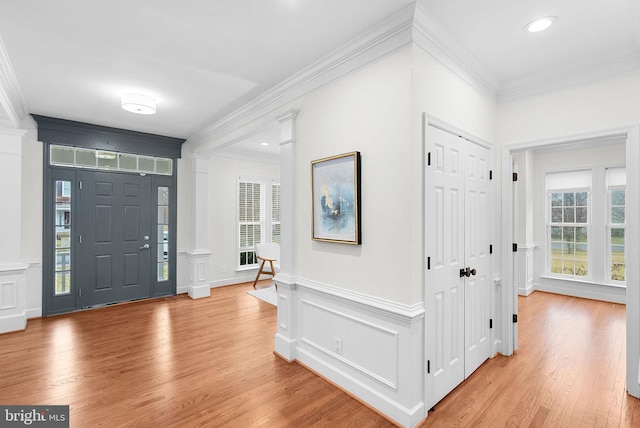 entrance foyer featuring crown molding, light wood-style flooring, and ornate columns