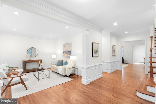 sitting room with light wood-style floors, ornamental molding, stairway, and ornate columns