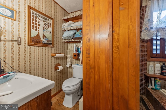 half bathroom with vanity, wood finished floors, toilet, and wallpapered walls