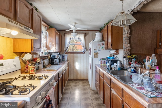 kitchen featuring white appliances, brown cabinets, a sink, and under cabinet range hood