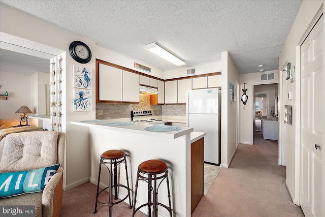 kitchen featuring white appliances, a peninsula, visible vents, and under cabinet range hood