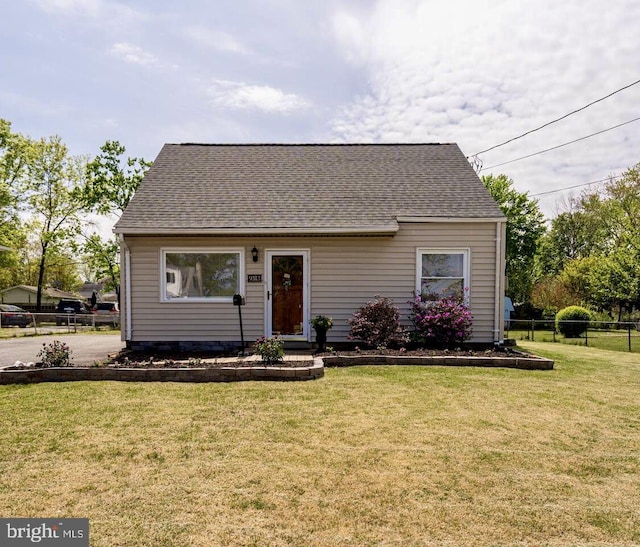 view of front of house with a shingled roof, a front lawn, and fence