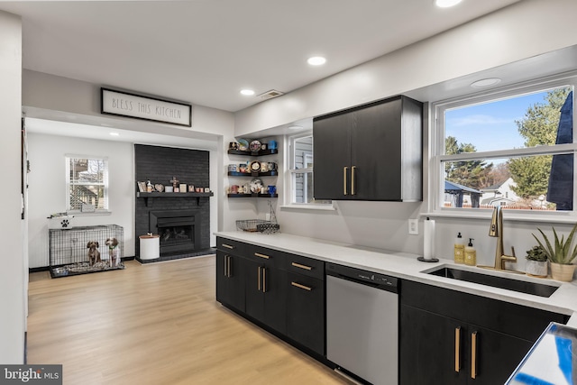 bar featuring light wood-style flooring, a fireplace, a sink, stainless steel dishwasher, and a wealth of natural light