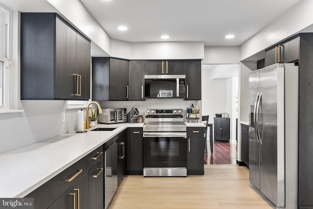 kitchen with light countertops, recessed lighting, light wood-style flooring, appliances with stainless steel finishes, and a sink