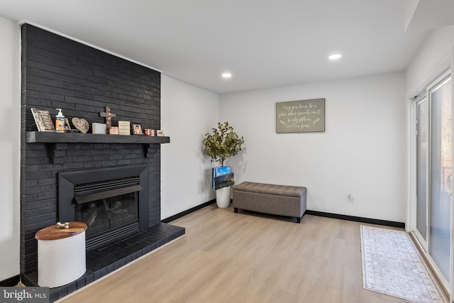 living area with recessed lighting, a brick fireplace, baseboards, and wood finished floors