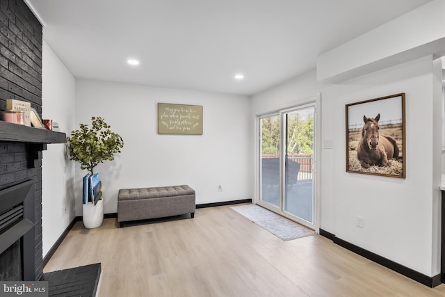 sitting room with light wood finished floors, recessed lighting, a brick fireplace, and baseboards