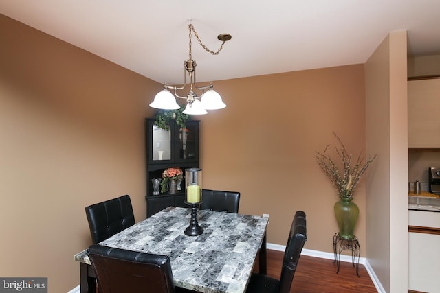 dining area with dark wood-style flooring, a notable chandelier, and baseboards