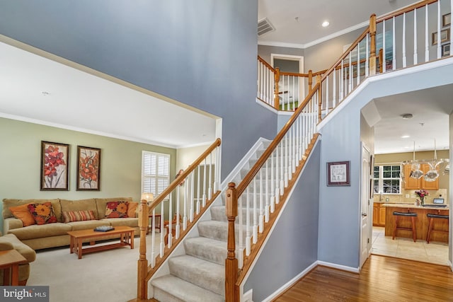 staircase with wood finished floors, baseboards, visible vents, a high ceiling, and ornamental molding