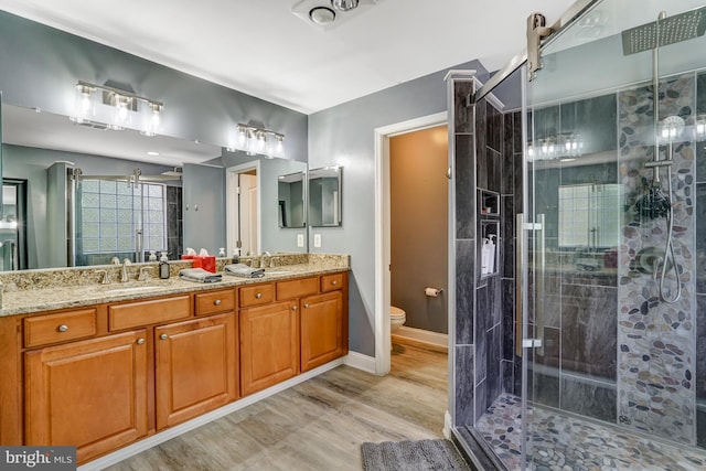 full bathroom featuring wood finished floors, double vanity, a sink, a shower stall, and toilet