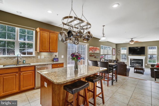 kitchen with a glass covered fireplace, light stone counters, light tile patterned floors, a sink, and stainless steel dishwasher