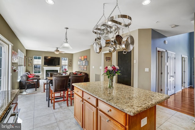 kitchen with light stone counters, light tile patterned flooring, recessed lighting, ceiling fan, and a glass covered fireplace