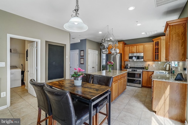 kitchen with a sink, tasteful backsplash, stainless steel appliances, brown cabinetry, and washer / dryer