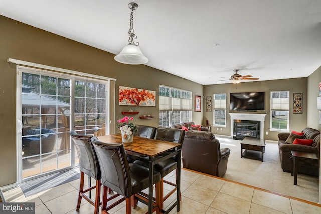 dining room with light carpet, a ceiling fan, a glass covered fireplace, light tile patterned flooring, and baseboards