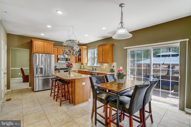 kitchen featuring backsplash, a center island, appliances with stainless steel finishes, light tile patterned floors, and light stone countertops