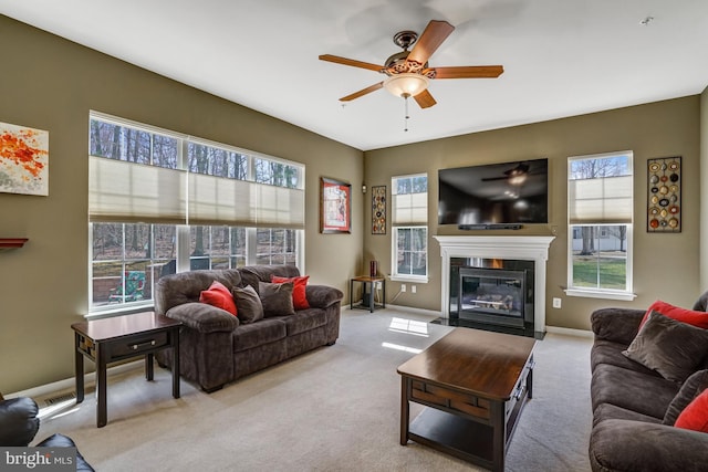 living area featuring a fireplace with flush hearth, baseboards, carpet floors, and ceiling fan