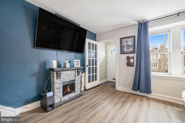 living room featuring a stone fireplace, baseboards, and wood finished floors