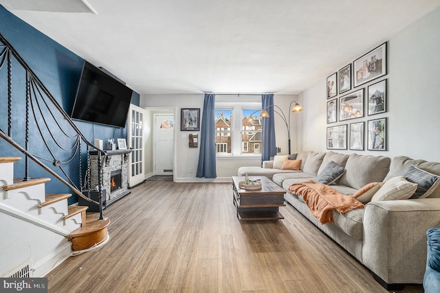 living room featuring baseboards, stairway, wood finished floors, and a stone fireplace