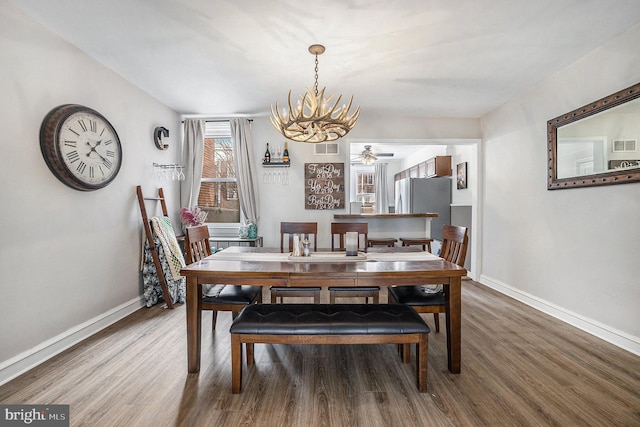 dining room featuring ceiling fan with notable chandelier, wood finished floors, visible vents, and baseboards