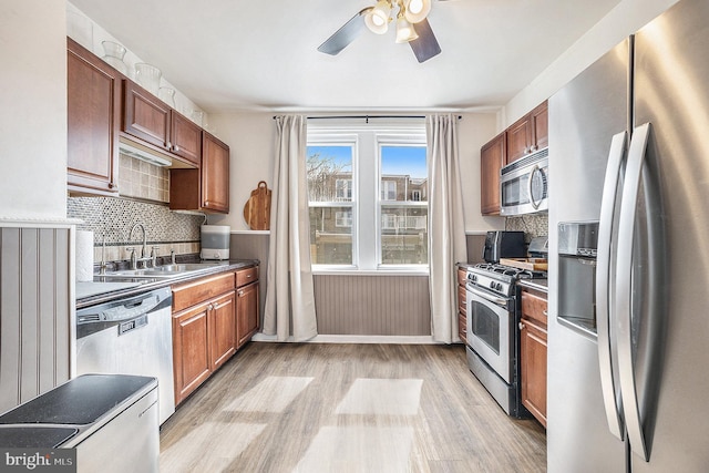 kitchen featuring stainless steel appliances, light wood-style flooring, decorative backsplash, a ceiling fan, and a sink