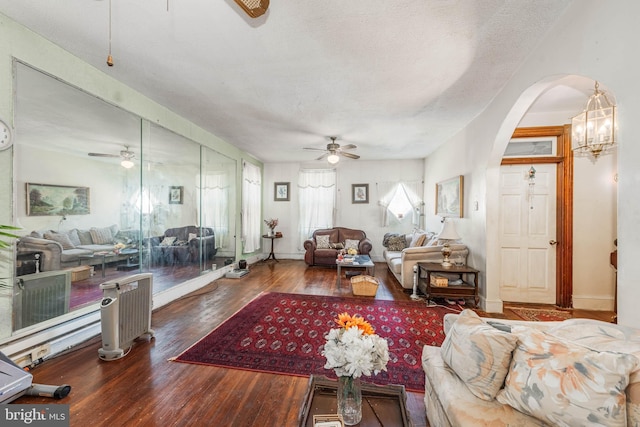 living area featuring arched walkways, a textured ceiling, ceiling fan with notable chandelier, and wood finished floors