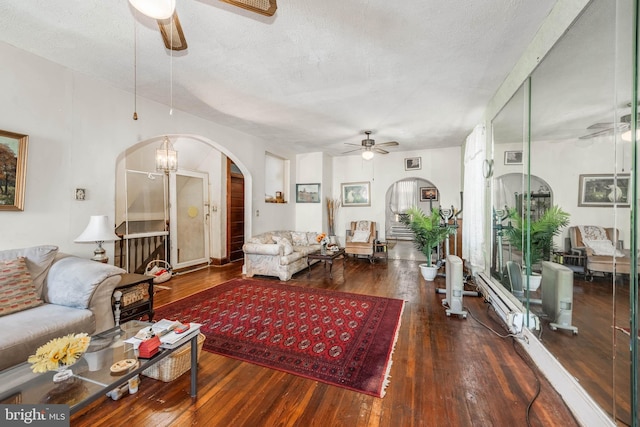 living area featuring wood-type flooring, arched walkways, a textured ceiling, and ceiling fan with notable chandelier