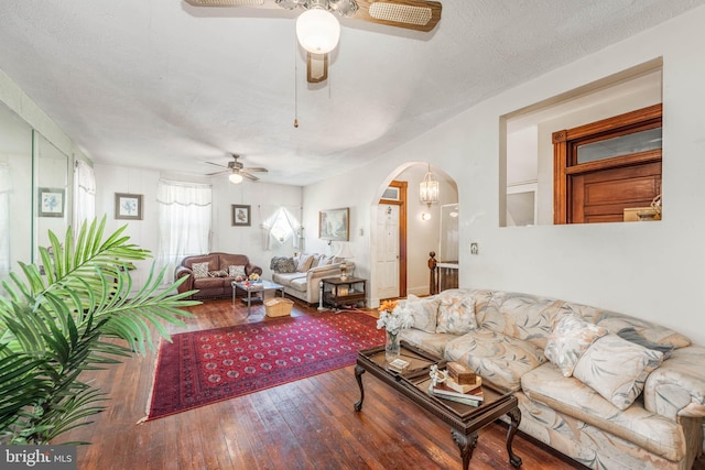 living room featuring hardwood / wood-style flooring, a textured ceiling, arched walkways, and a ceiling fan