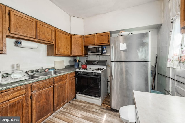 kitchen with a sink, appliances with stainless steel finishes, light wood-style floors, and brown cabinets