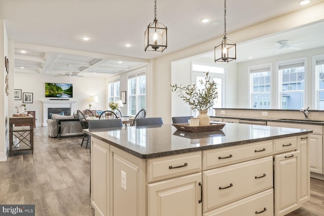 kitchen with a fireplace, a sink, a kitchen island, coffered ceiling, and light wood-style floors