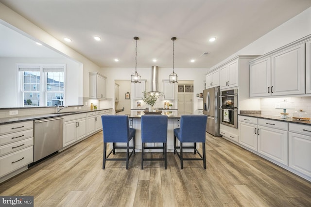 kitchen featuring light wood-style flooring, wall chimney exhaust hood, a breakfast bar, a center island, and stainless steel appliances