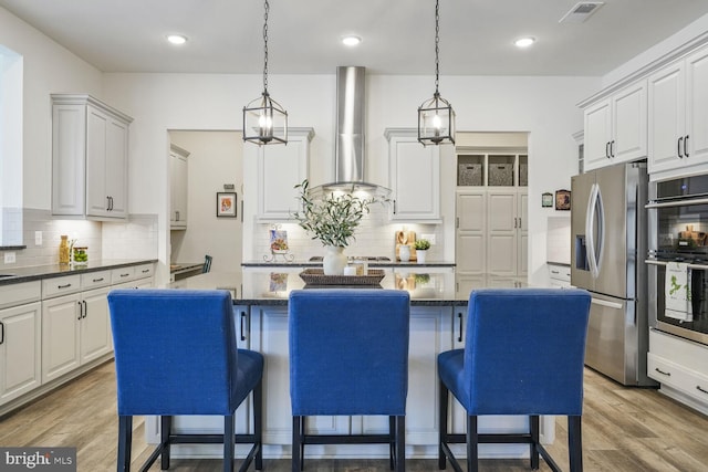 kitchen with a kitchen island, visible vents, wall chimney range hood, appliances with stainless steel finishes, and light wood-type flooring