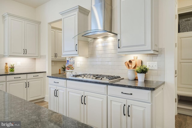 kitchen with wood finished floors, white cabinetry, wall chimney range hood, backsplash, and stainless steel gas stovetop