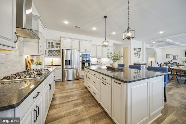 kitchen with a center island, visible vents, appliances with stainless steel finishes, wood finished floors, and wall chimney exhaust hood