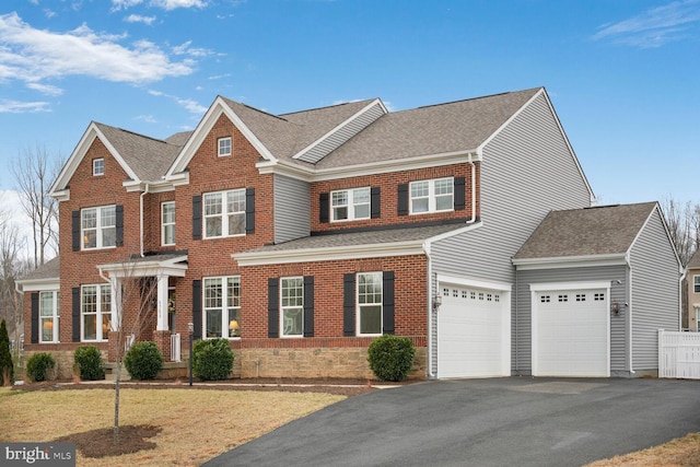 colonial home with a garage, aphalt driveway, a shingled roof, and brick siding