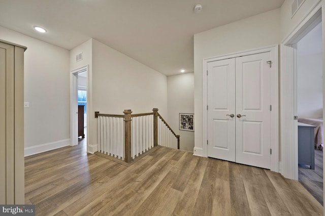 corridor with visible vents, light wood finished floors, an upstairs landing, and baseboards