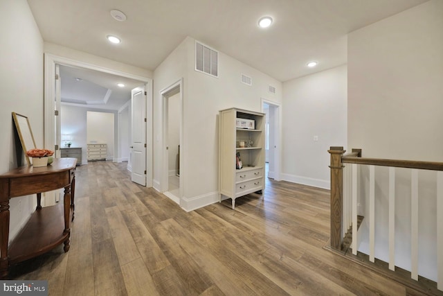 hall featuring baseboards, visible vents, an upstairs landing, and wood finished floors