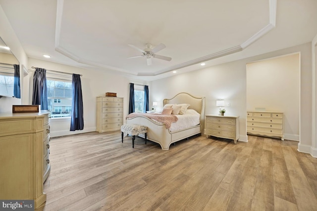 bedroom with a tray ceiling, multiple windows, light wood-style flooring, and baseboards