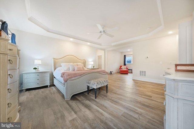 bedroom with crown molding, a raised ceiling, visible vents, light wood-style floors, and baseboards