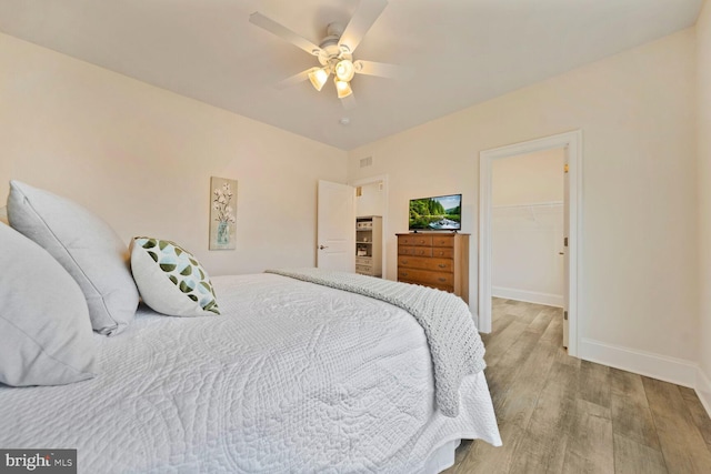 bedroom with baseboards, light wood-style flooring, ceiling fan, a spacious closet, and a closet