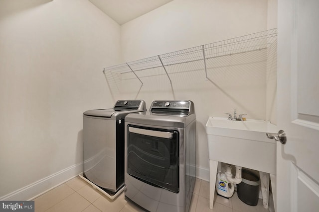 clothes washing area featuring laundry area, light tile patterned flooring, washing machine and clothes dryer, and baseboards