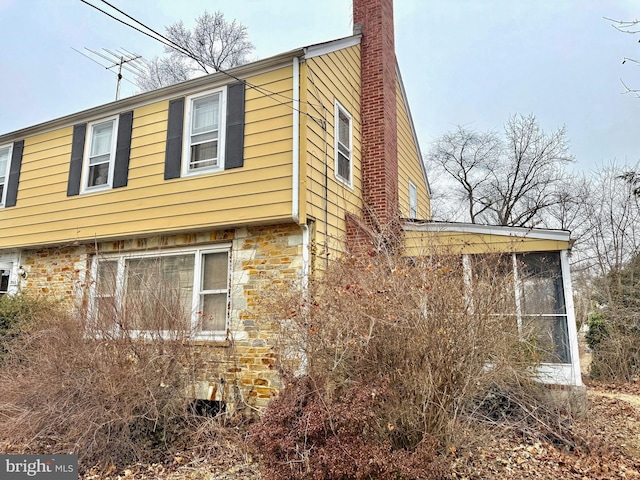 view of property exterior featuring stone siding, a sunroom, and a chimney